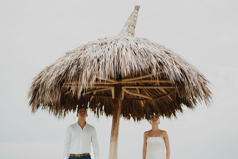 The couple standing under a beachside palapa, embracing the peaceful surroundings