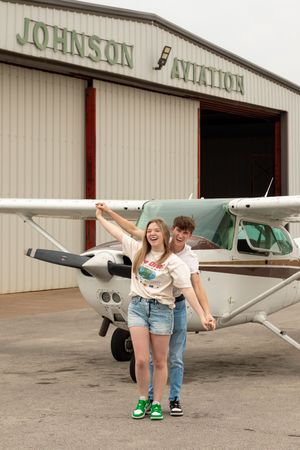 A playful couple poses in front of a small aircraft at Johnson Aviation hangar. Couples Session. East Texas, Fort Worth Texas, Dallas Texas