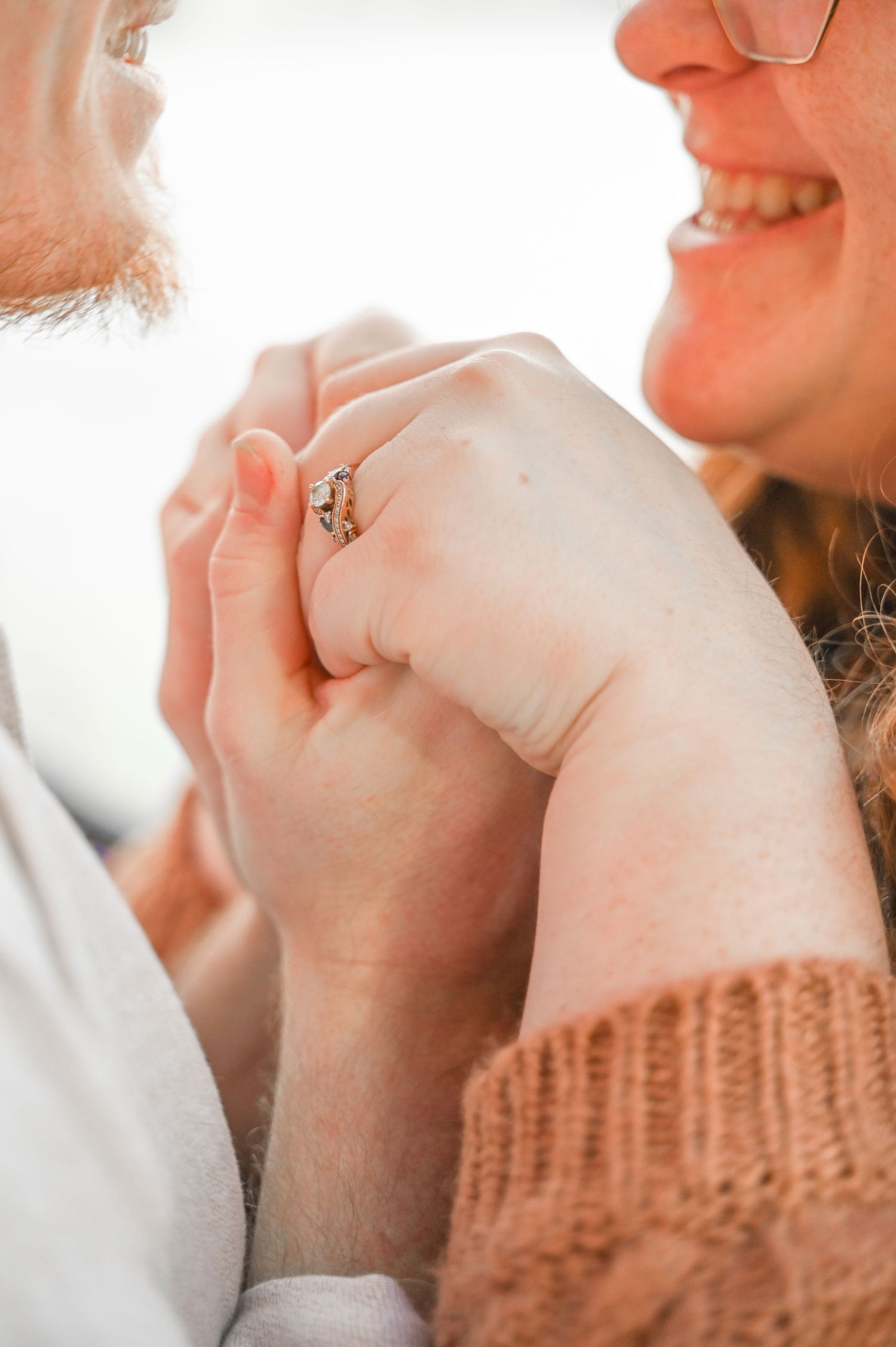 Close-up of couple's hands with engagement ring in warm sunlight.