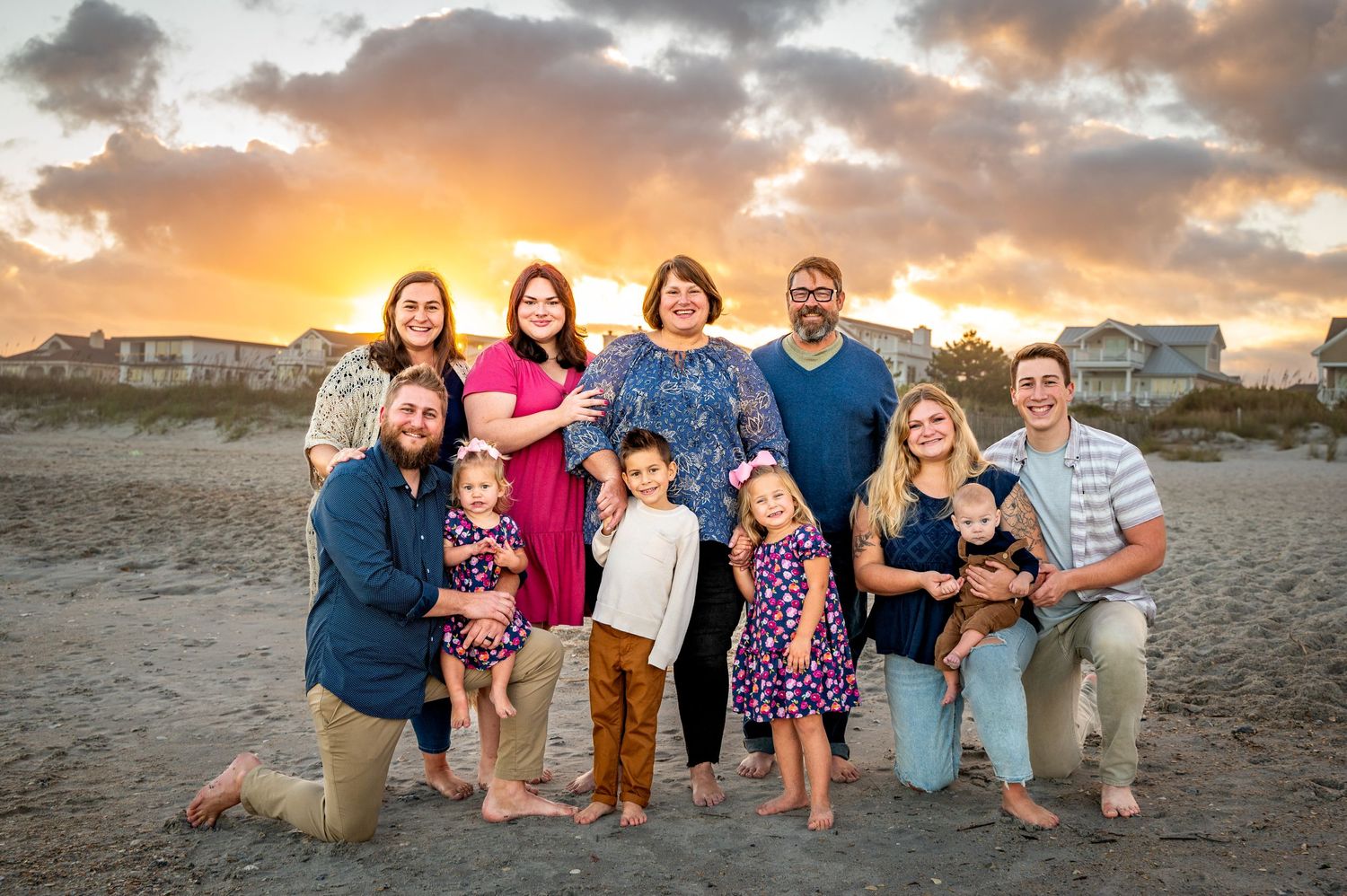 Extended family group portrait on beach at sunset with colorful sky background.