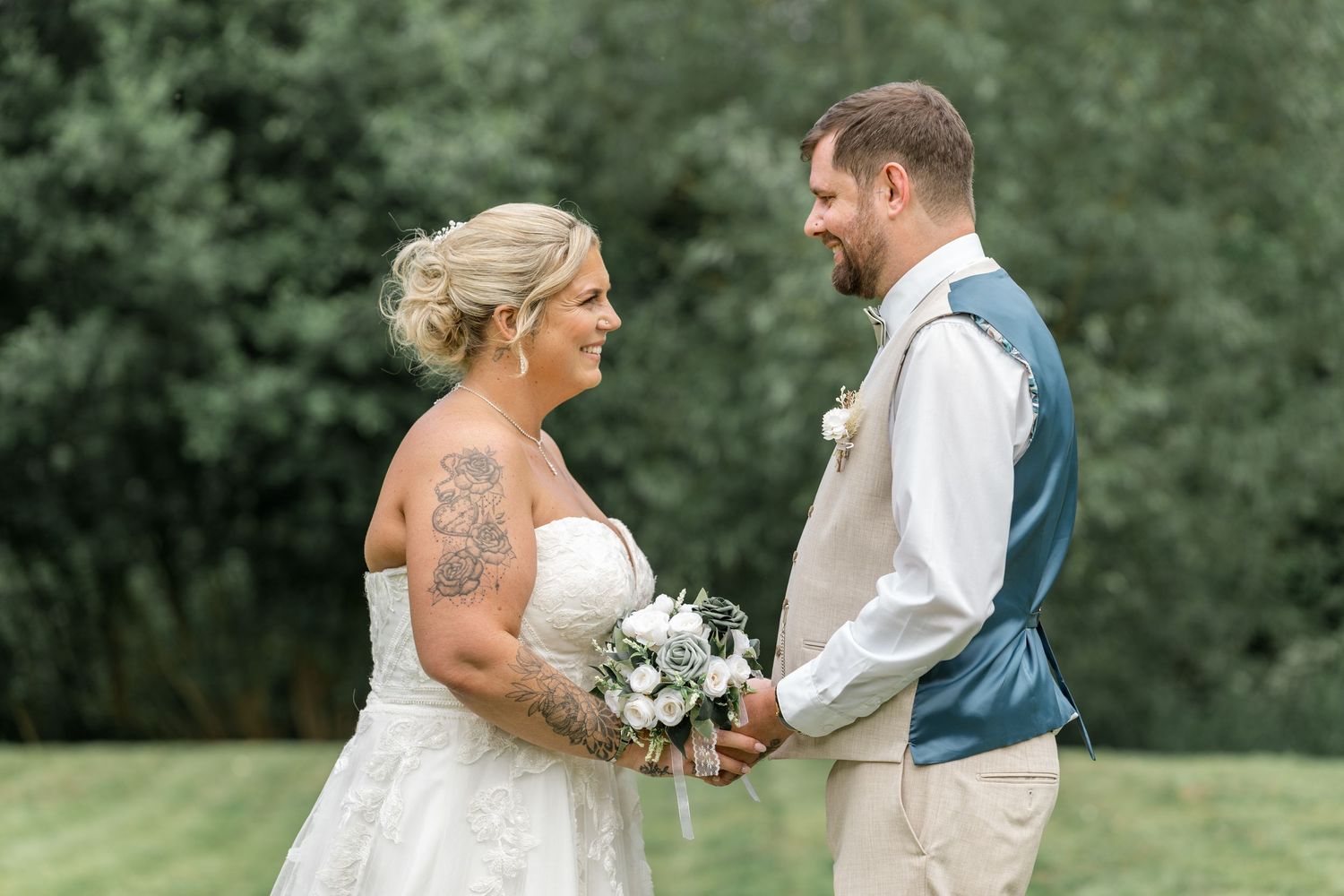Couple poses together outdoors during their wedding ceremony surrounded by lush greenery.