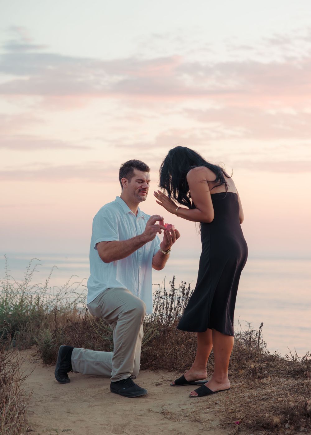 Romantic proposal scene at sunset overlooking the ocean as a couple shares a special moment on the cliffside.