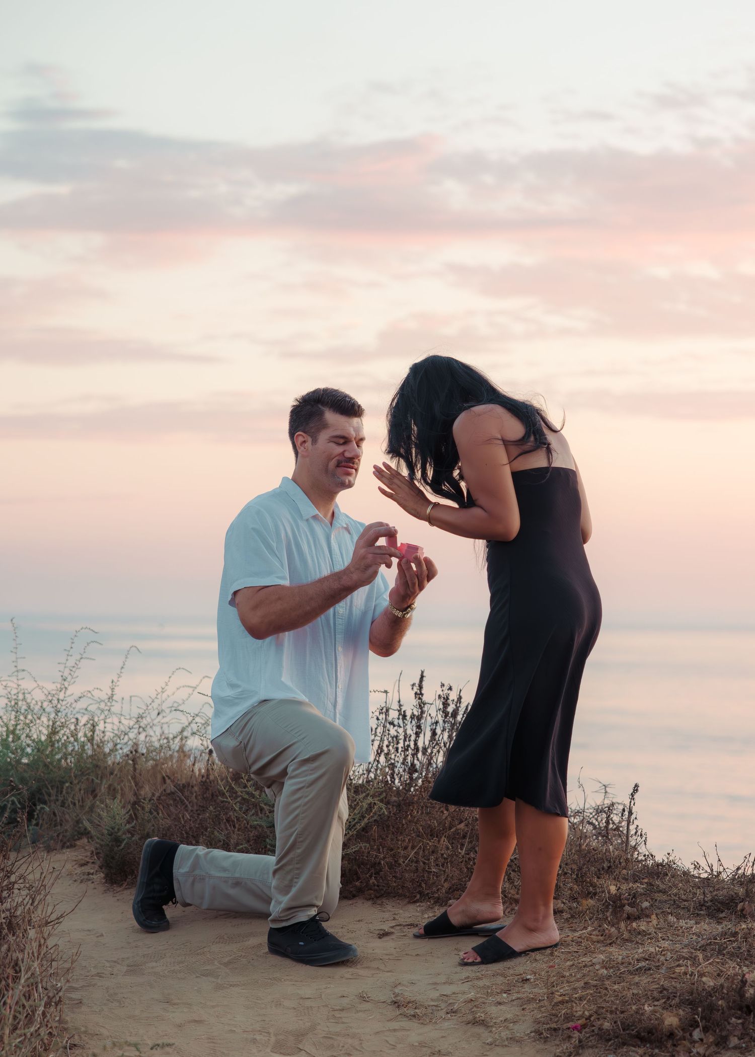 Romantic proposal scene at sunset overlooking the ocean as a couple shares a special moment on the cliffside.