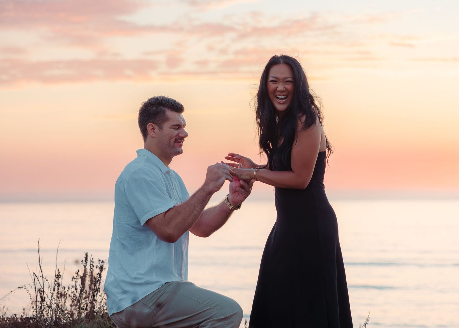 Surprise proposal moment at sunset by the ocean with joyful reaction.