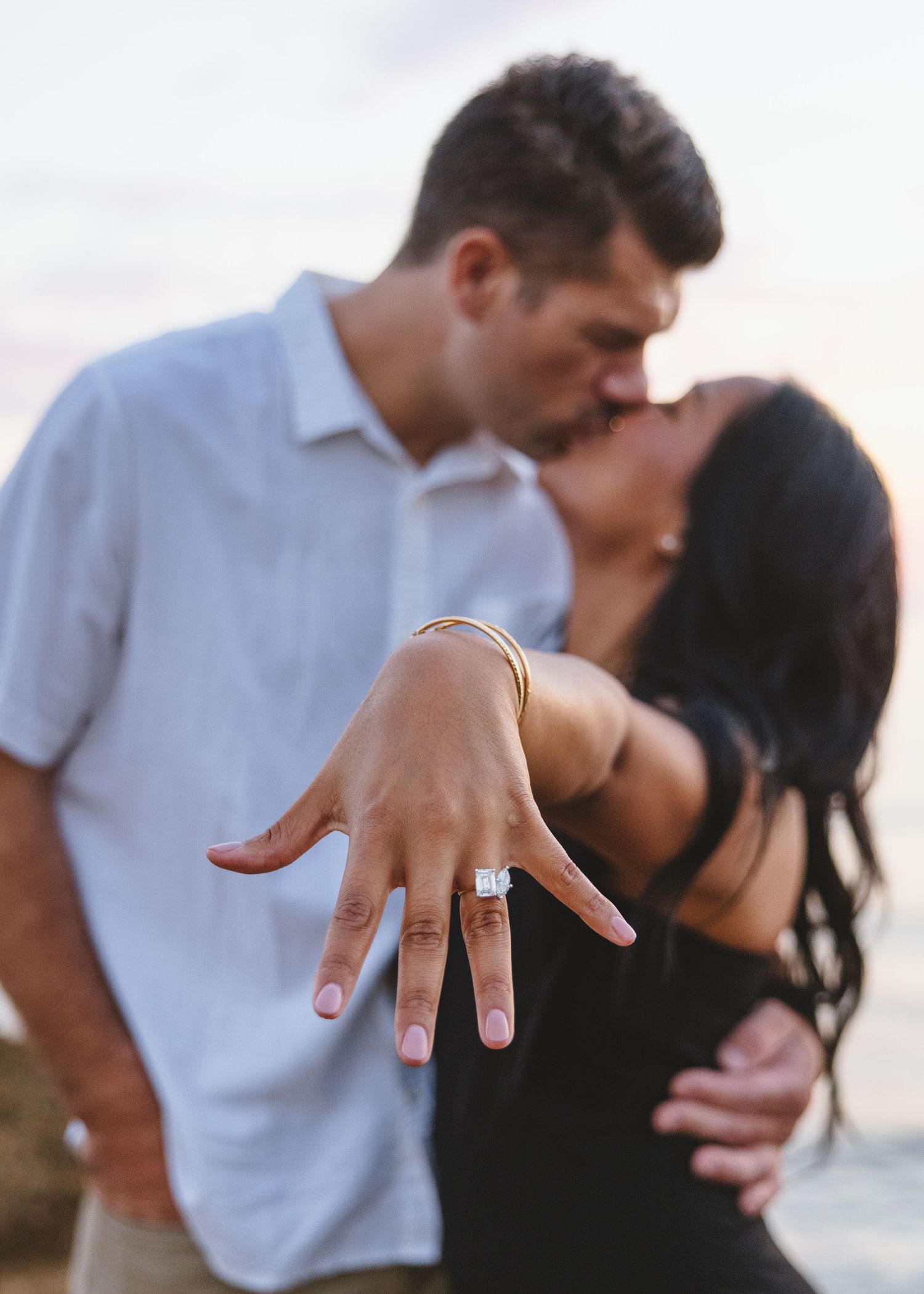 Close-up of a sparkling engagement ring as couple shares intimate moment by the ocean.