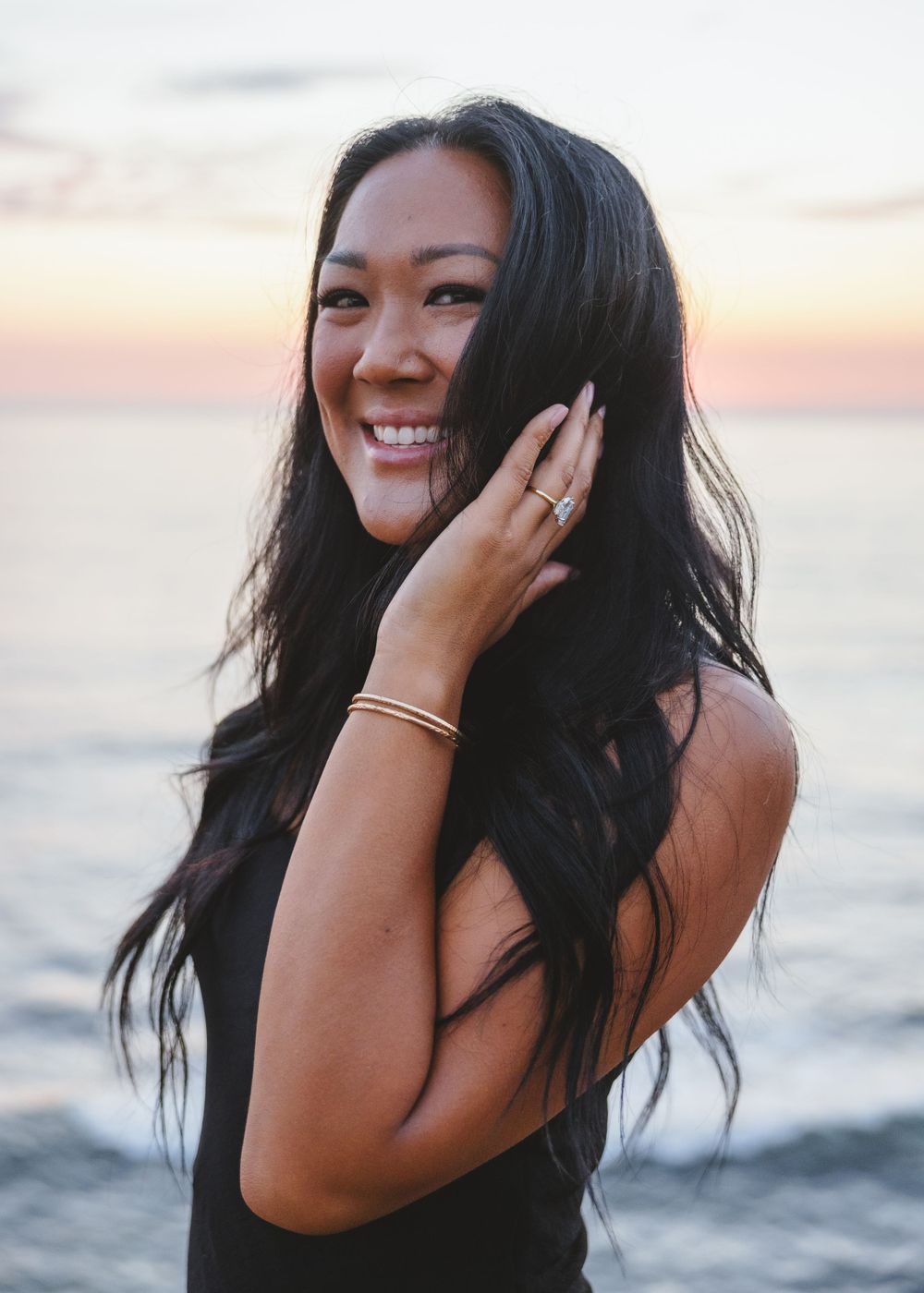 Joyful woman showing off her engagement ring at sunset by the ocean.