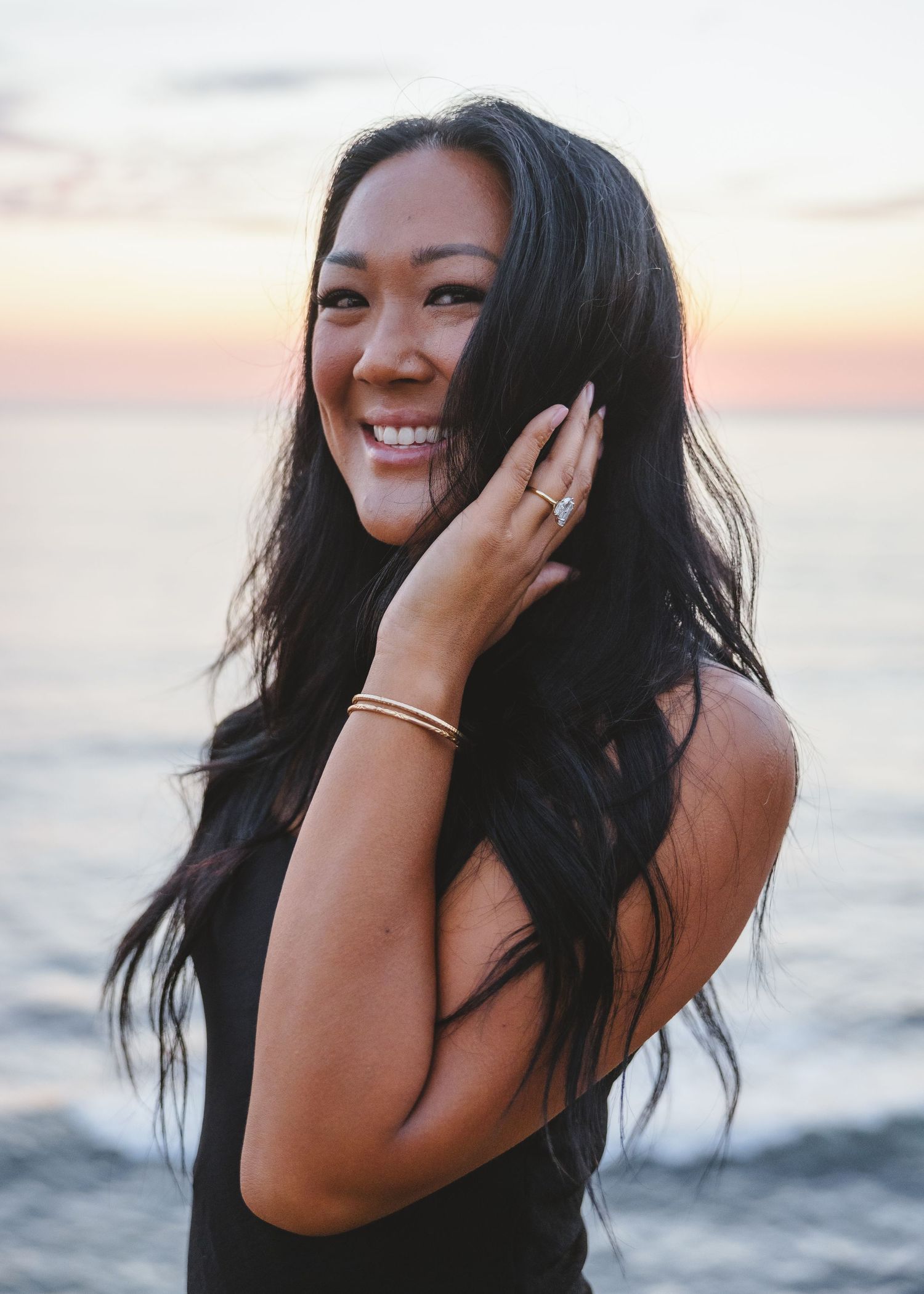 Joyful woman showing off her engagement ring at sunset by the ocean.