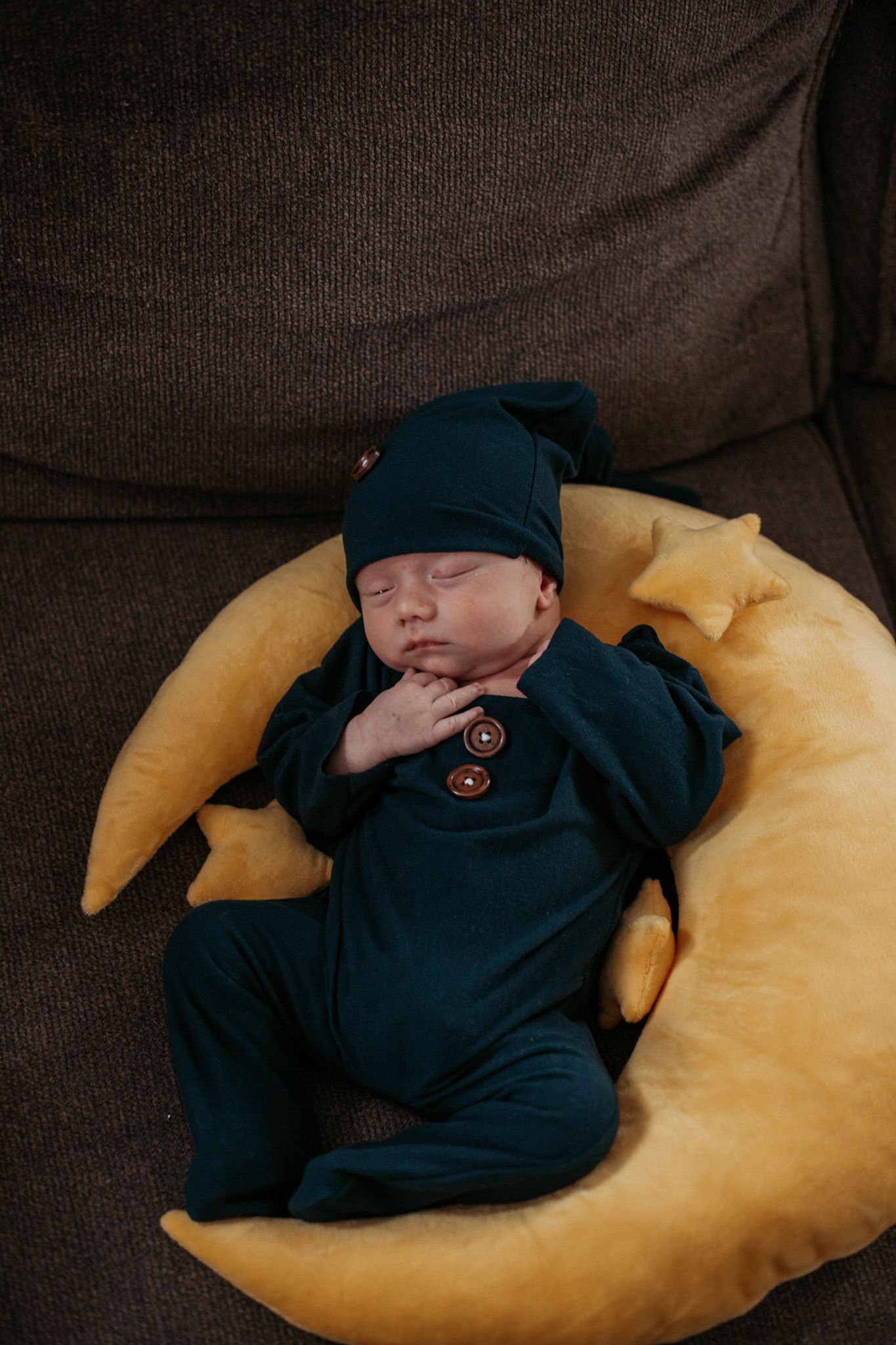 Sleeping newborn wearing navy outfit on curved yellow pillow.