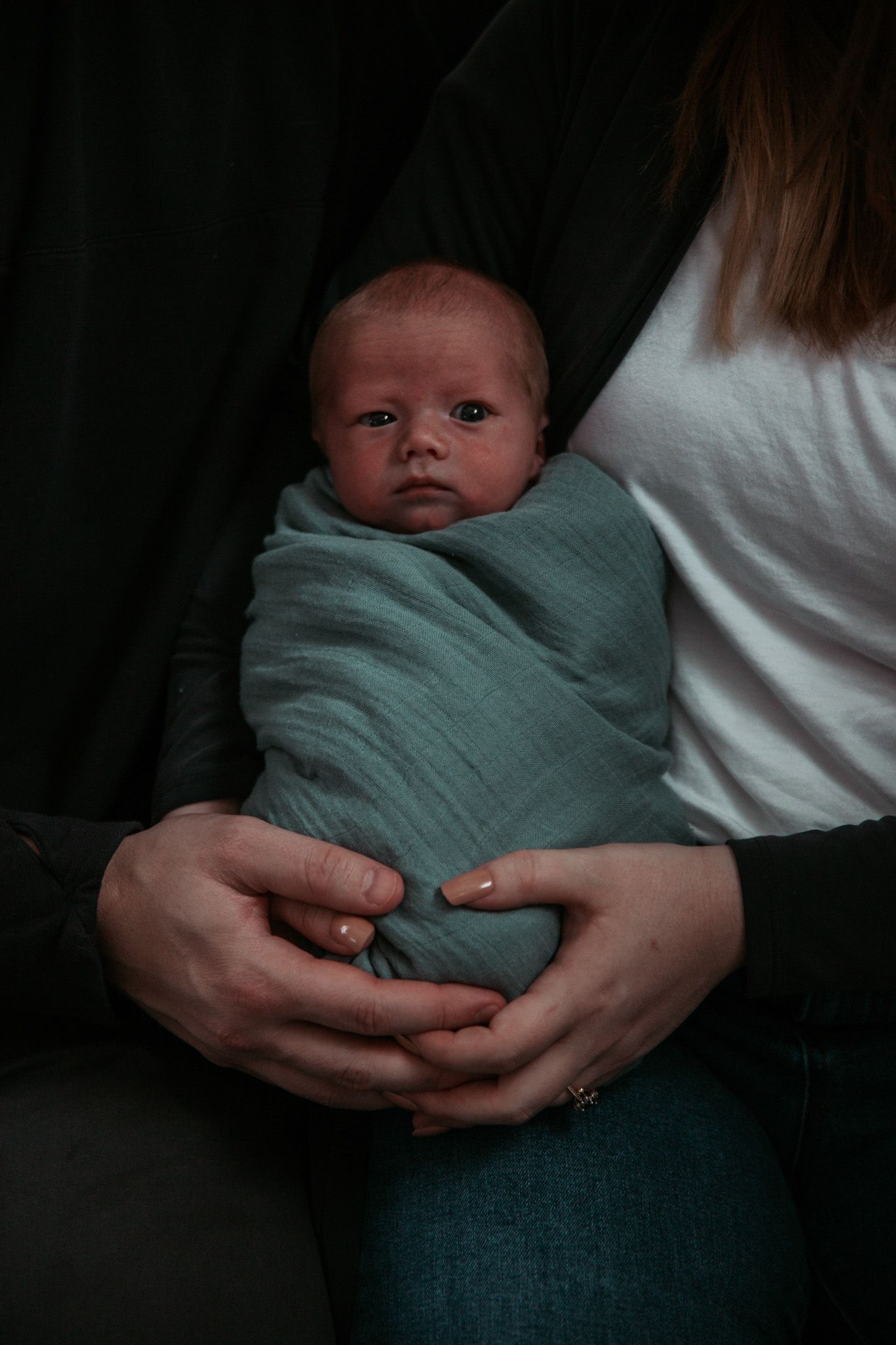 Newborn baby wrapped in teal blanket held in gentle embrace.