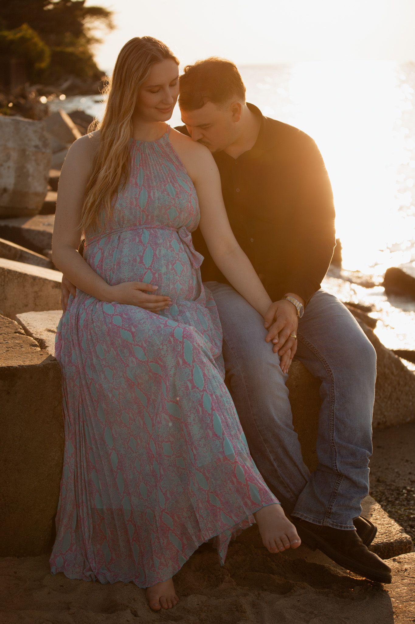 Couple sits together on rocky beach during golden hour.
