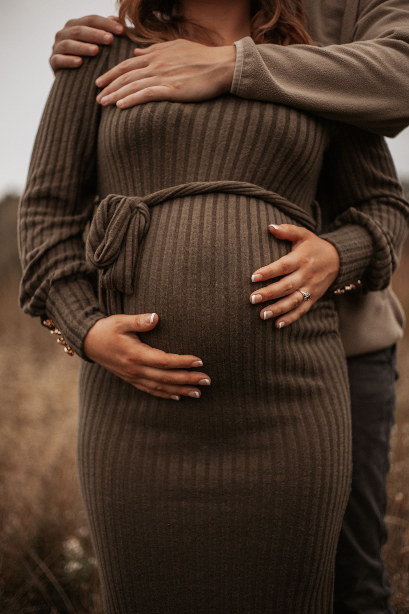Close-up shots of hands cradling pregnant belly in brown knit dress.