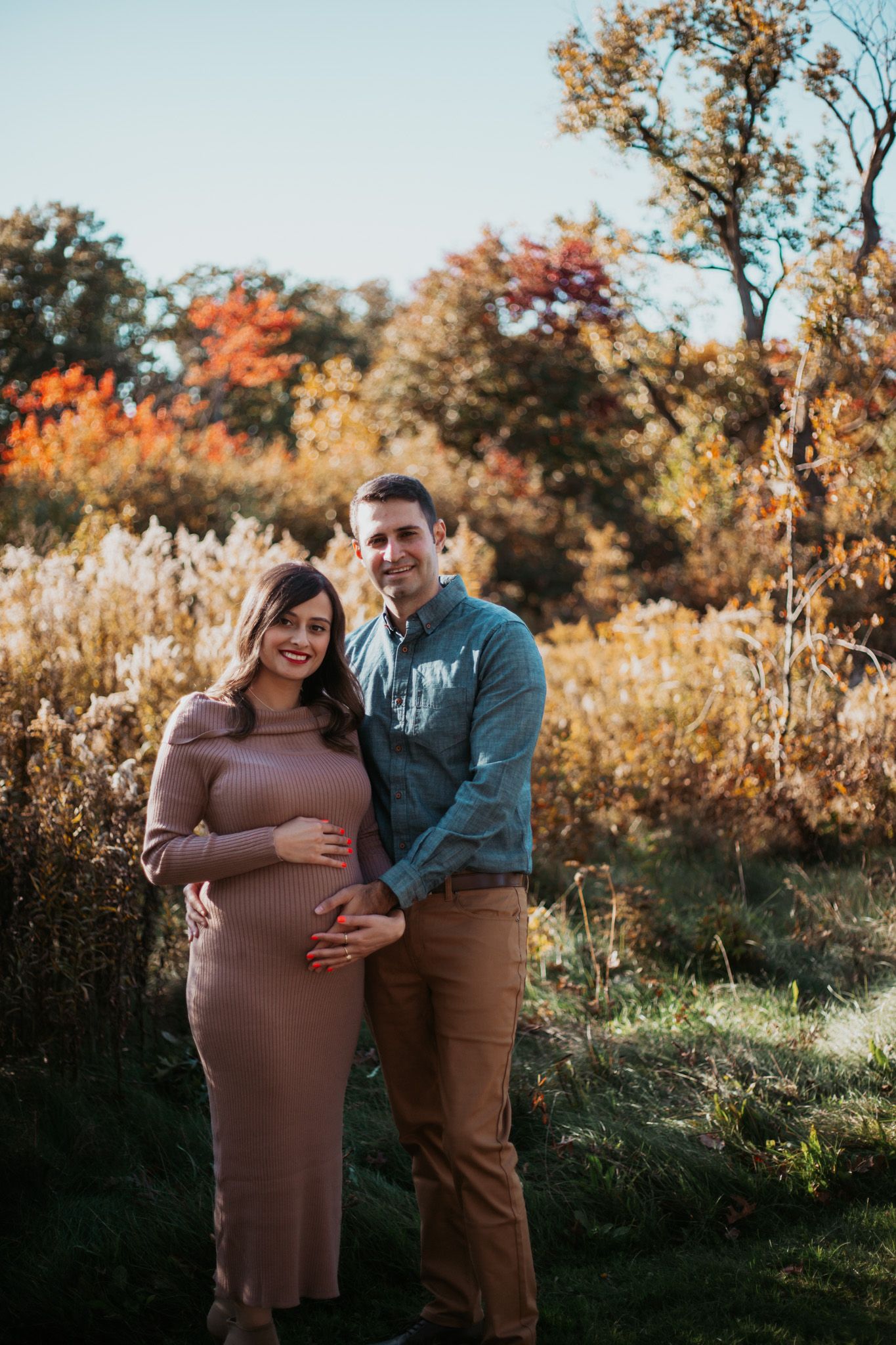 Maternity photo of expectant couple embracing in autumn field with fall foliage.