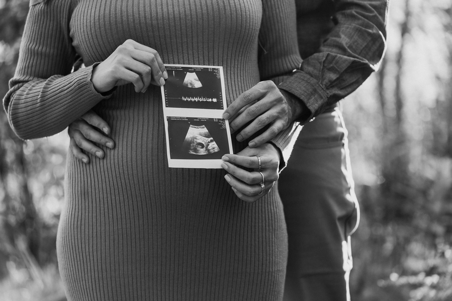 Black and white photo of couple holding ultrasound photos during pregnancy announcement shoot.
