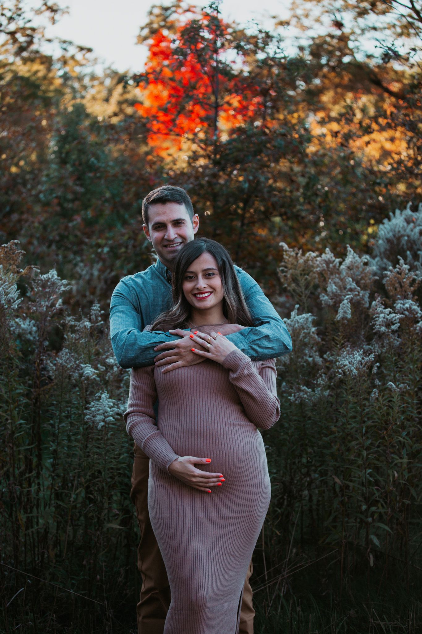 Maternity portrait of couple embracing at sunset with vibrant fall colors in background.