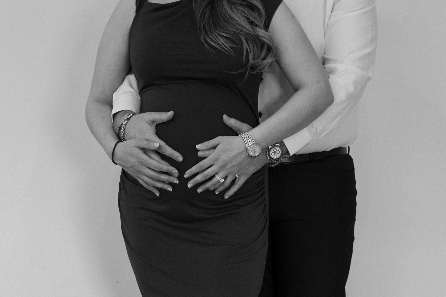 Intimate maternity photo session with couple in formal wear against white background.