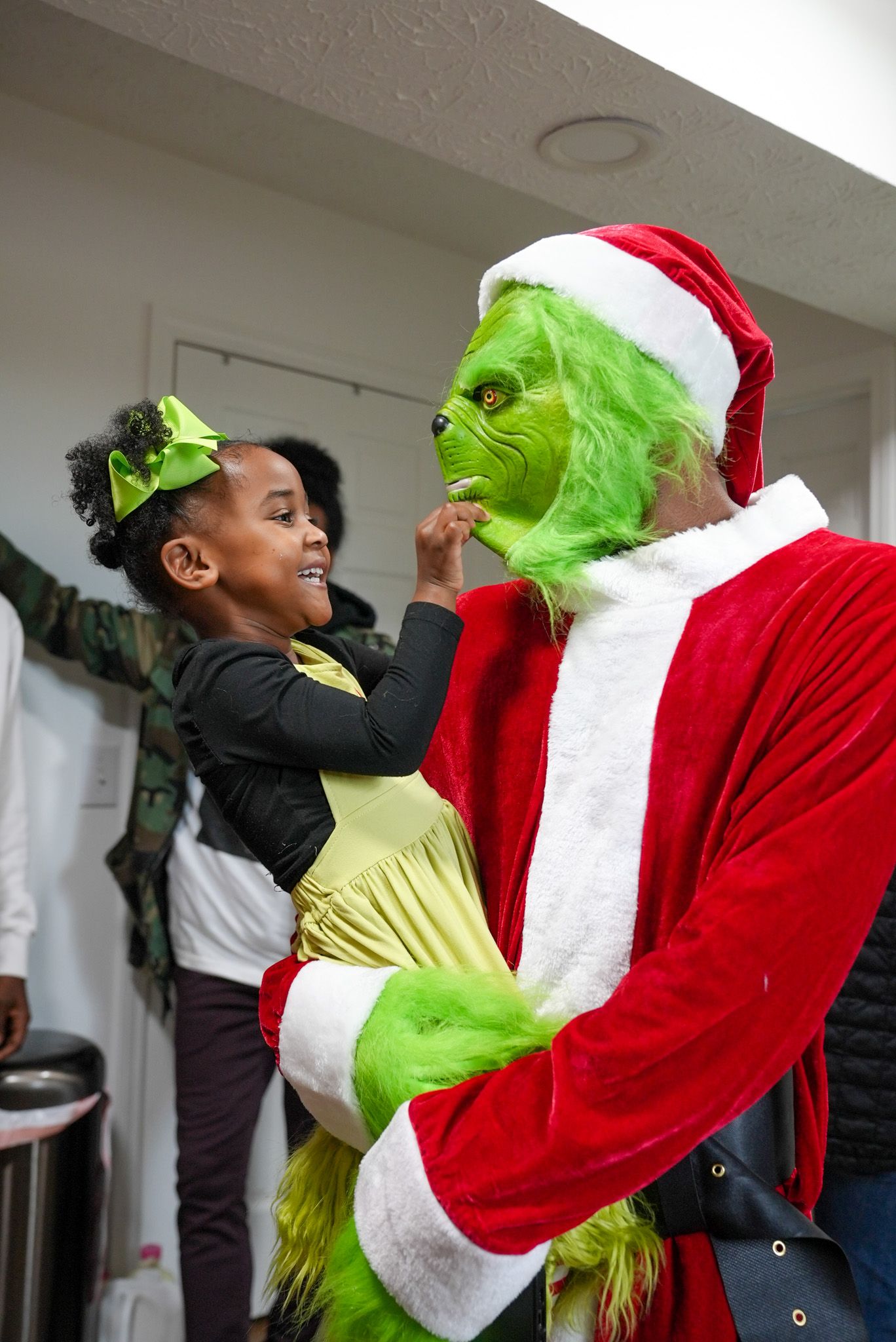 Young girl interacting with person dressed in Grinch costume at a festive Christmas event.