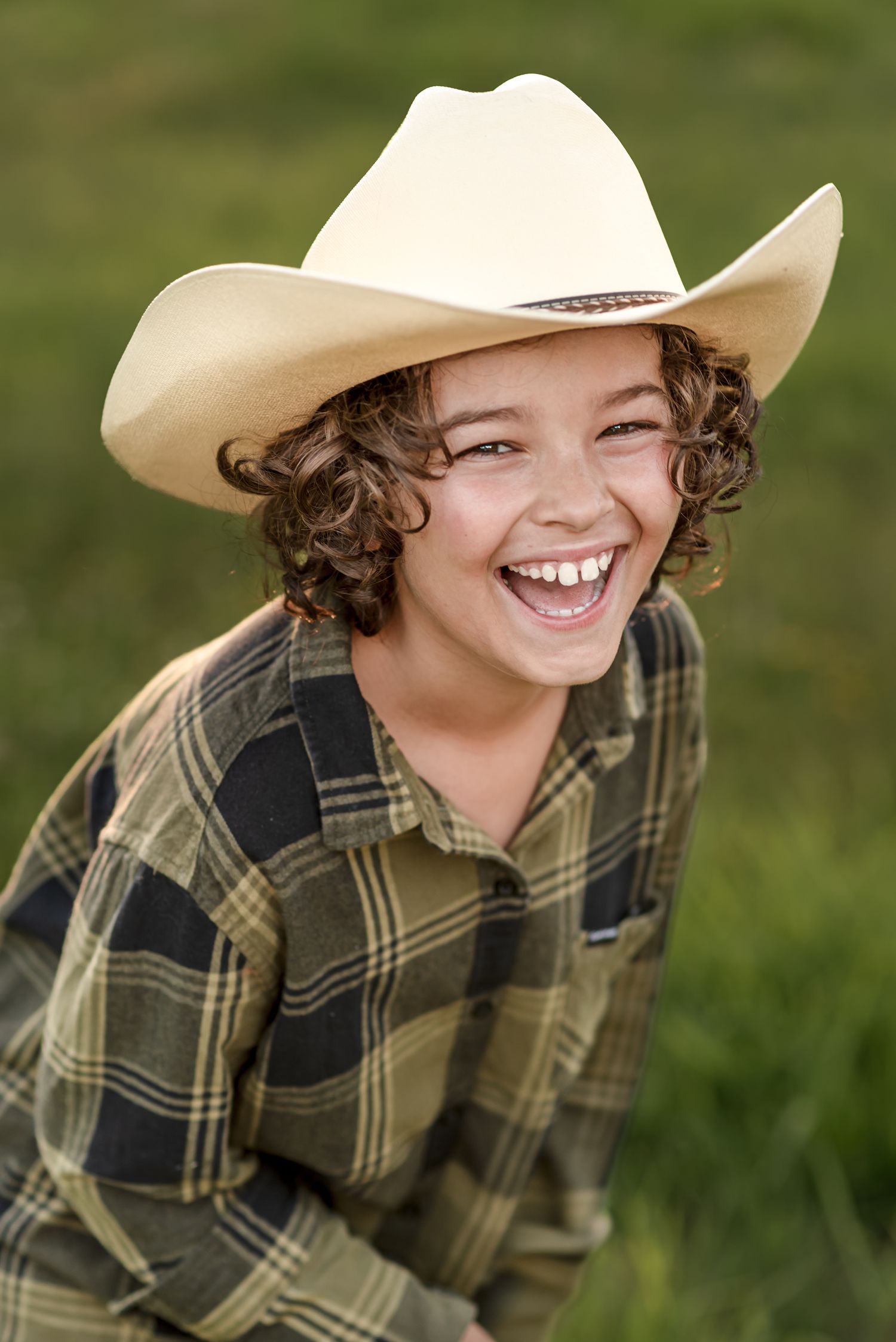 Someone wearing a cowboy hat and plaid shirt laughs joyfully outdoors.
