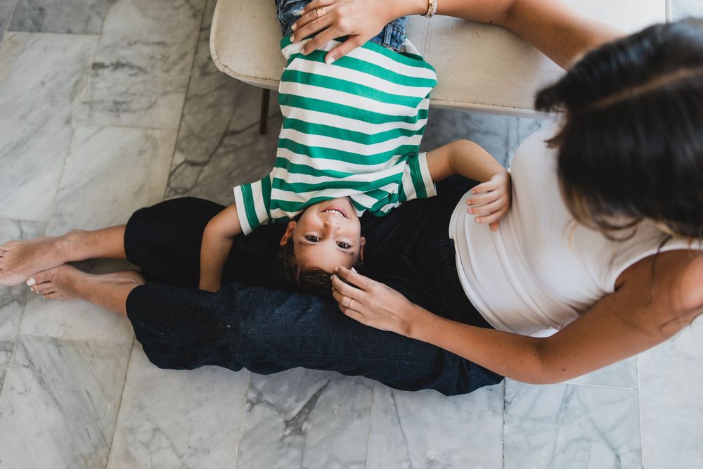A couple shares a tender moment lying on a white marble floor while wearing casual clothes.