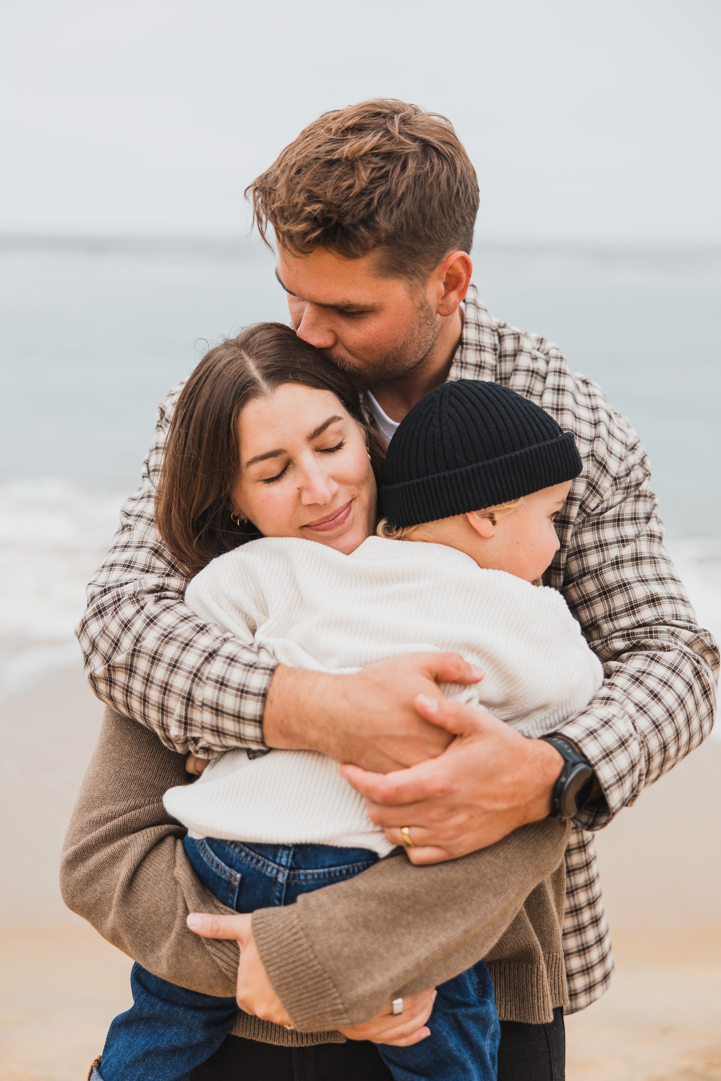 A couple embraces tenderly on a peaceful beach with cloudy skies in the background.