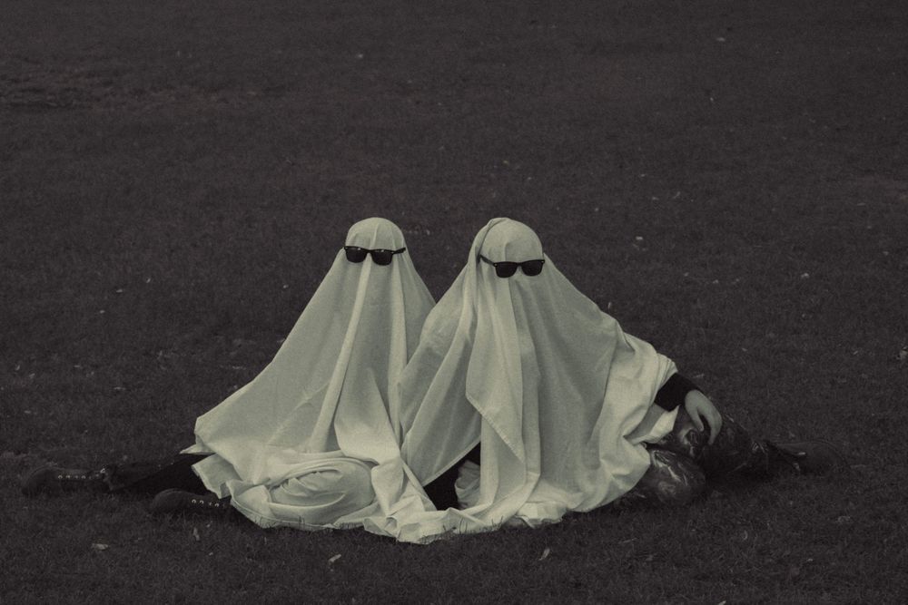 Two ghost figures with sunglasses sitting close together on dark ground.