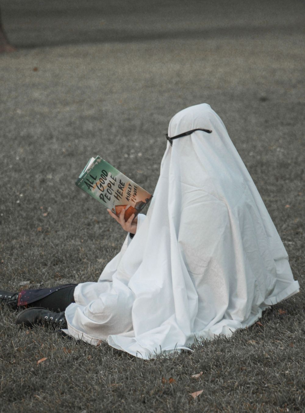 Ghost figure in white sheet with sunglasses sits on ground with beverage can.