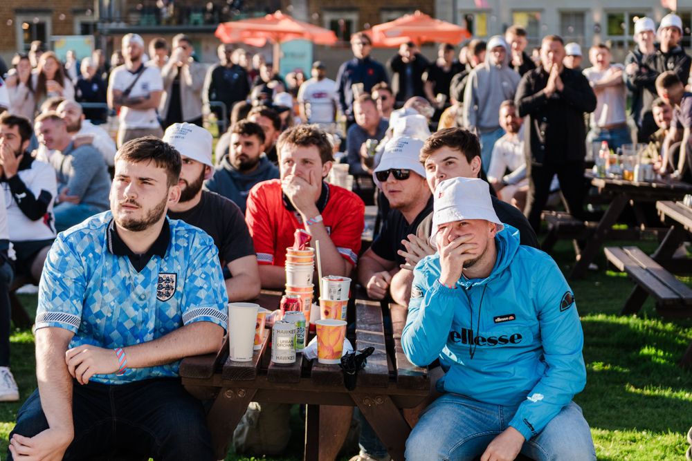 Large crowd of people sitting outdoors at a beer garden enjoying drinks and socializing on a sunny day.
