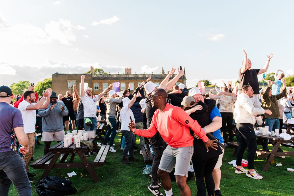 A group of people enjoying an outdoor event with lawn chairs and umbrellas on a grassy area.