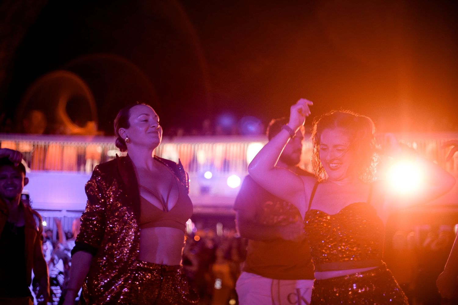 Silhouettes of party-goers dancing under colorful lights at nighttime cruise event.