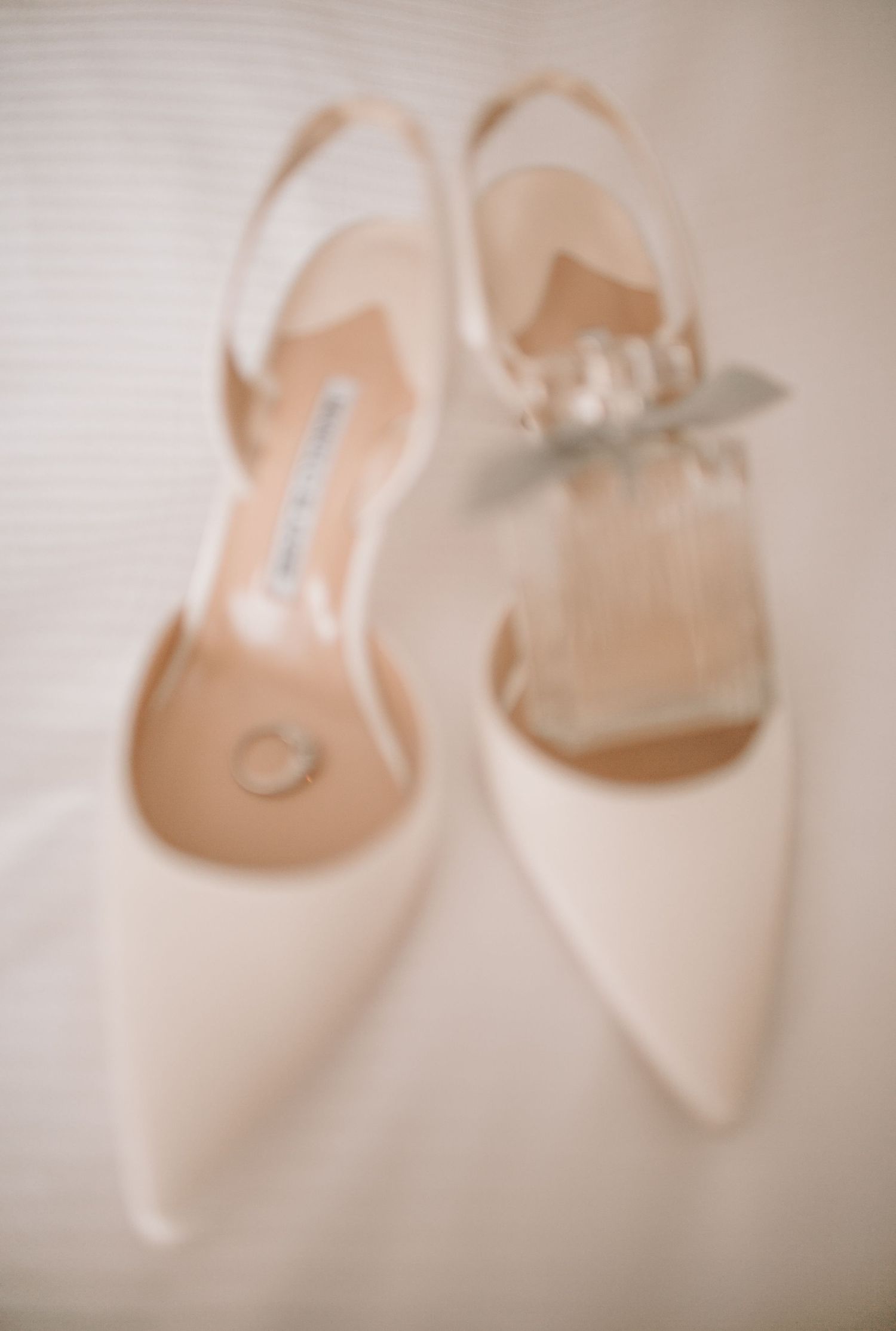 Elegant white bridal shoes with pointed toes displayed in a soft focus artistic arrangement.