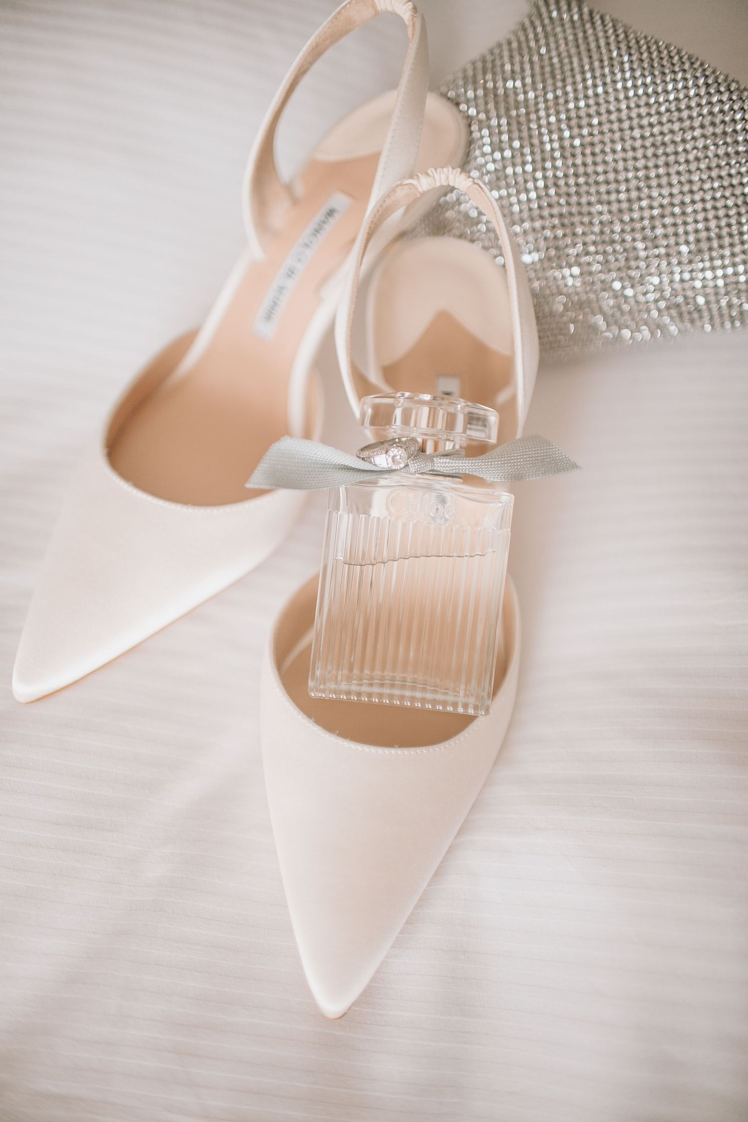 Bridal shoes photographed next to sparkling silver accessories in soft lighting.