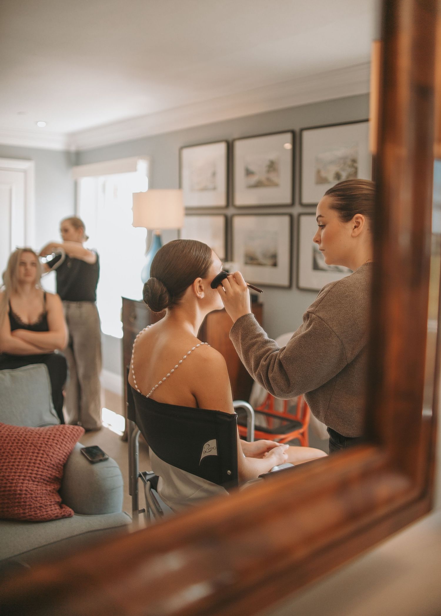 Wedding preparation scene captured through wooden mirror frame in warm tones.