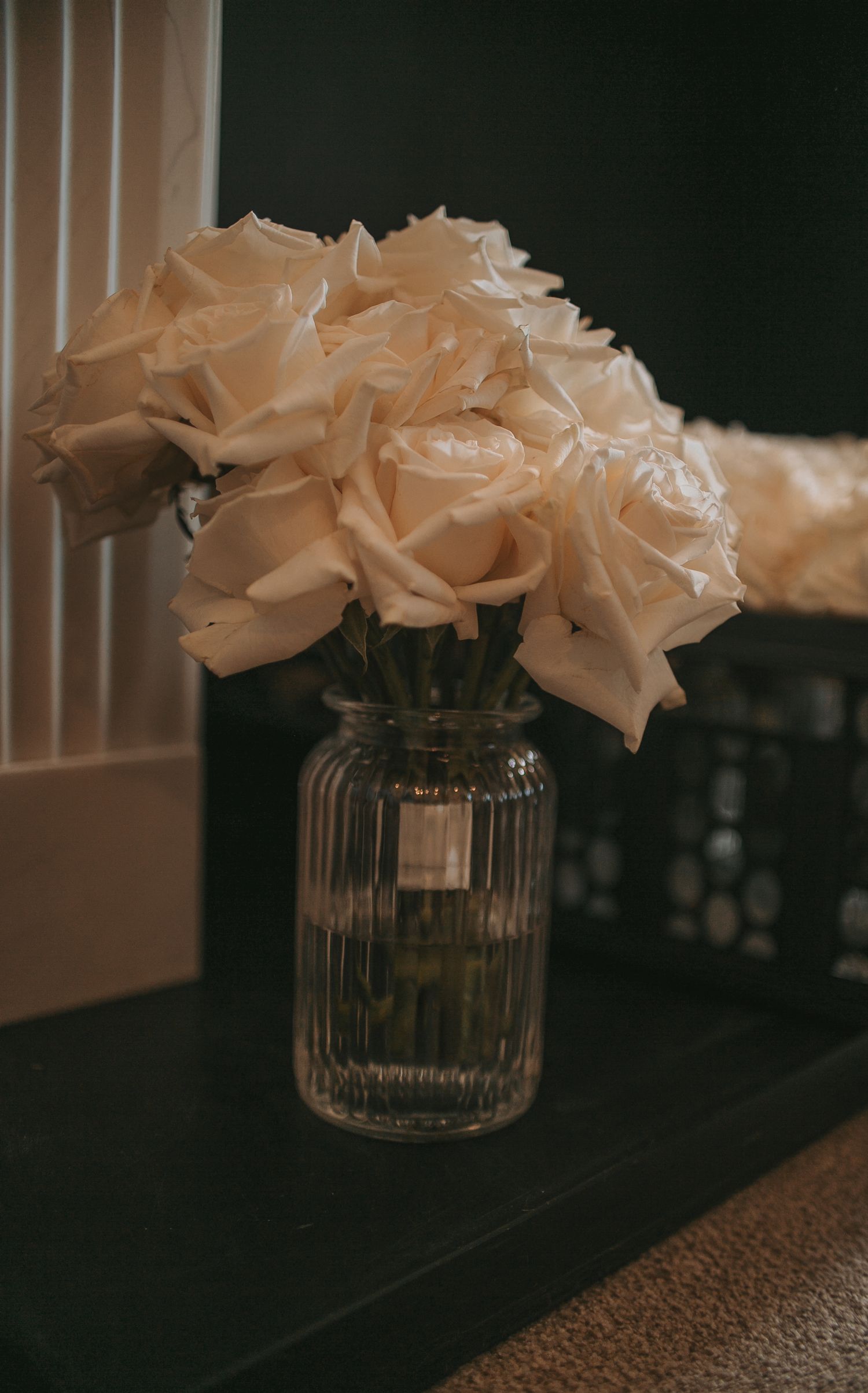 White roses arranged in a glass vase against a dark background.