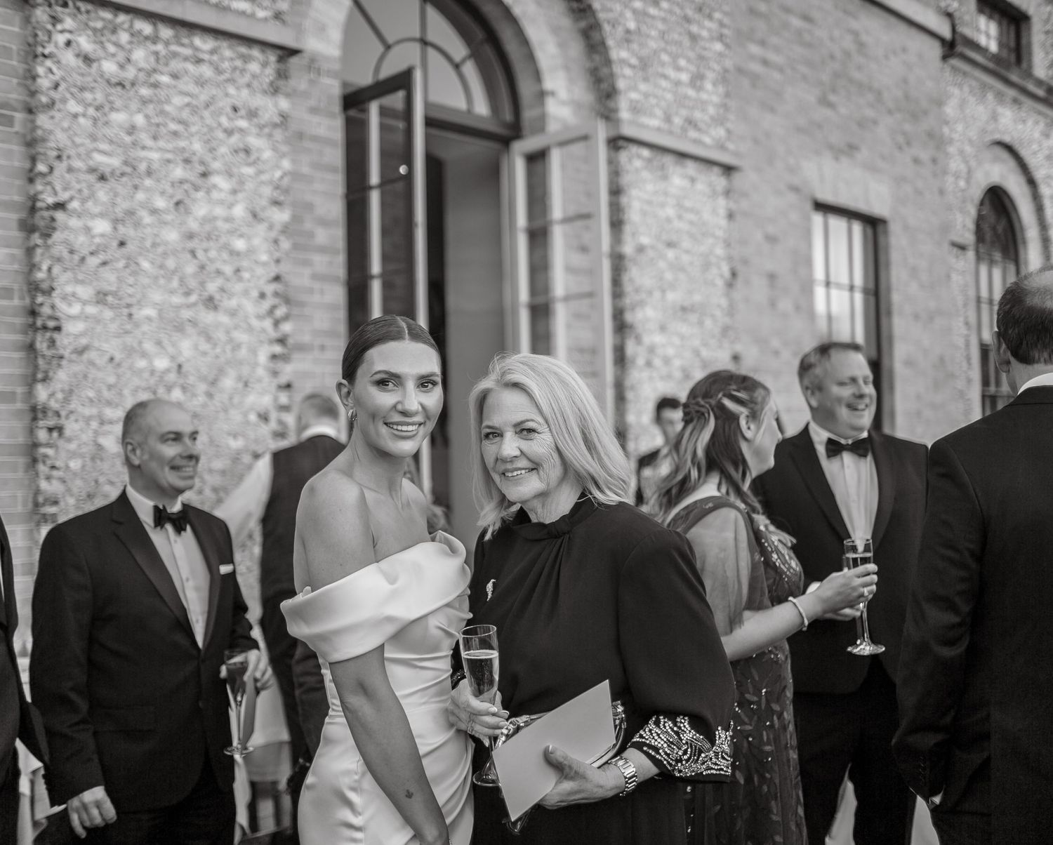 Wedding guests in formal attire gathered outside a historic stone building.