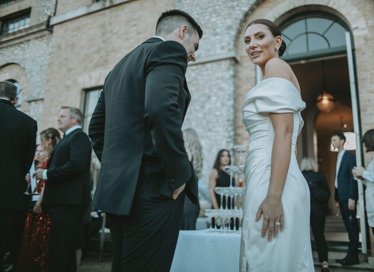 Wedding party members socializing outside a classic stone building.