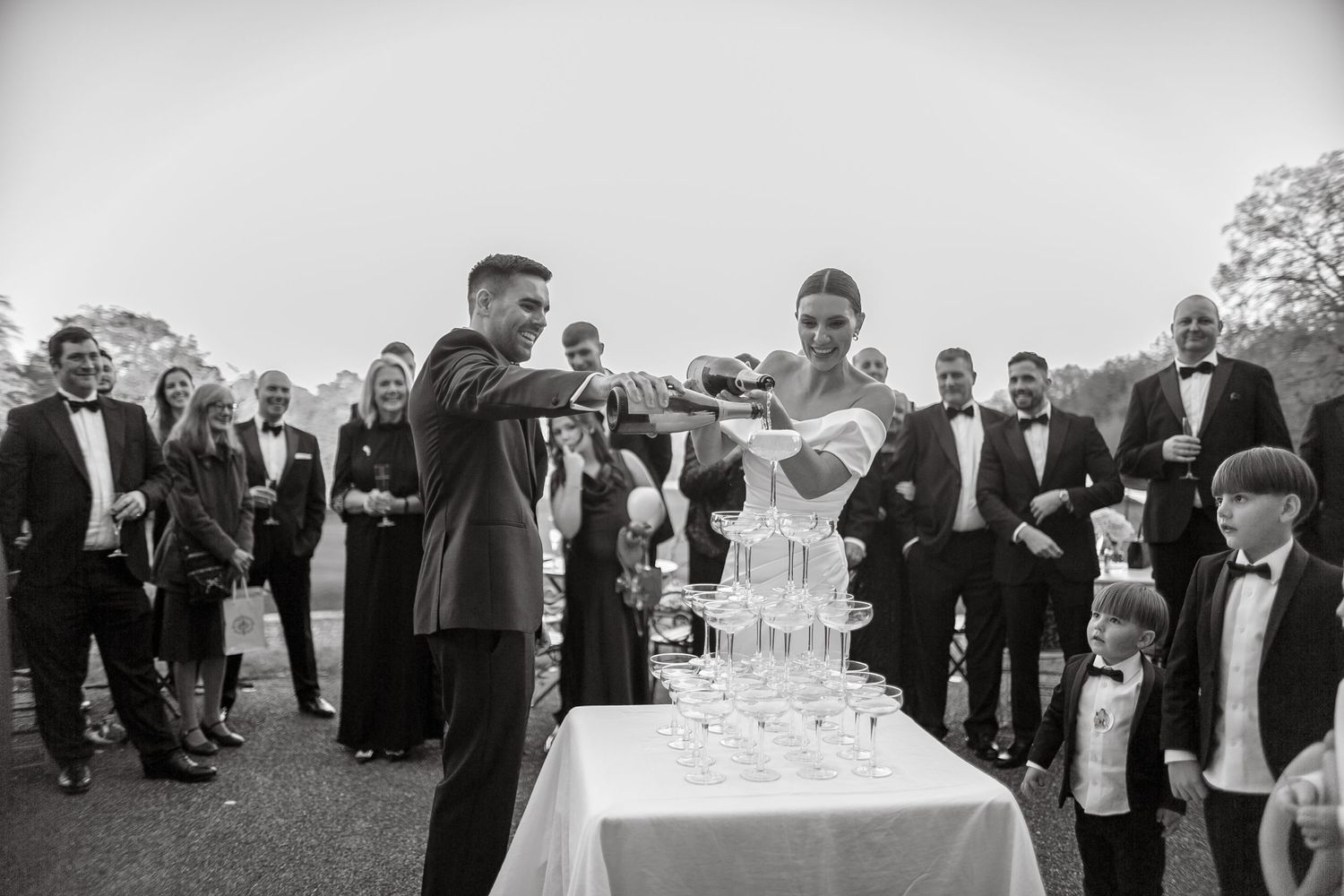 Black and white photo of guests enjoying drinks at an outdoor wedding reception.
