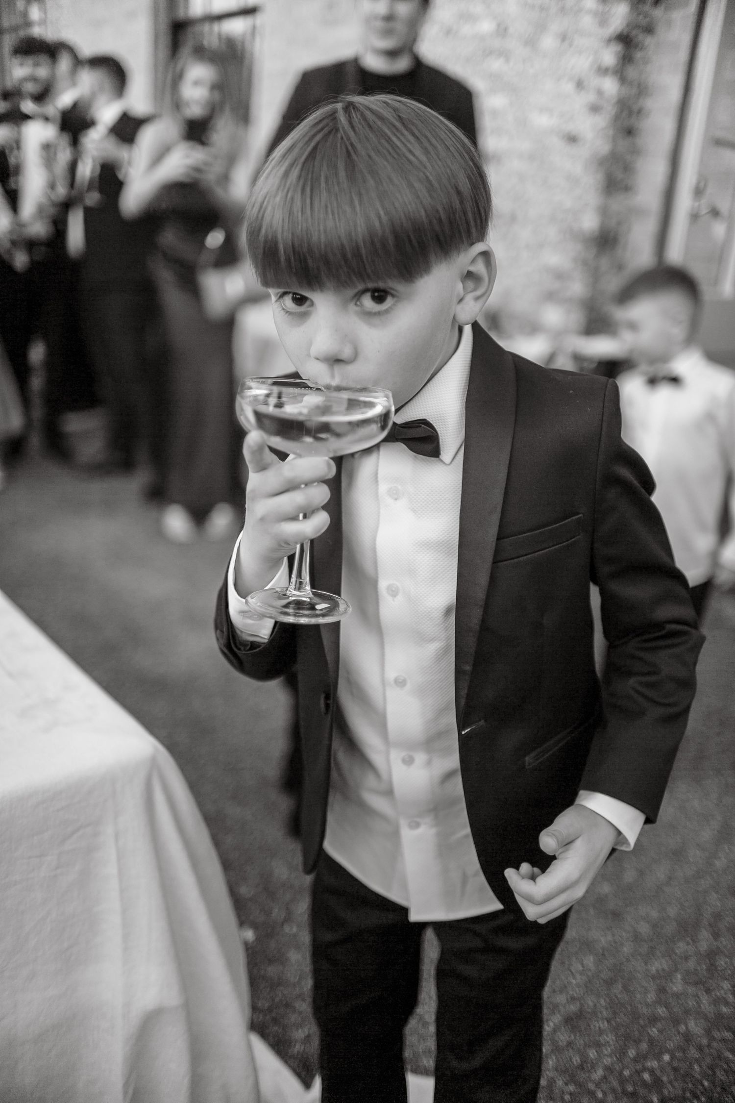 Young attendee in formal attire sips from a champagne coupe at a wedding reception.