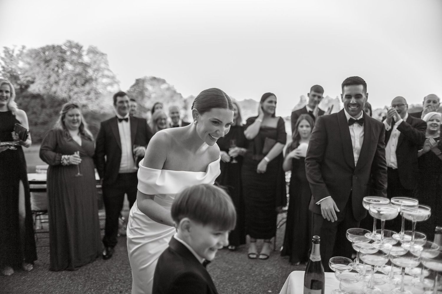 Guests observe the pouring of a champagne tower at an elegant outdoor event.