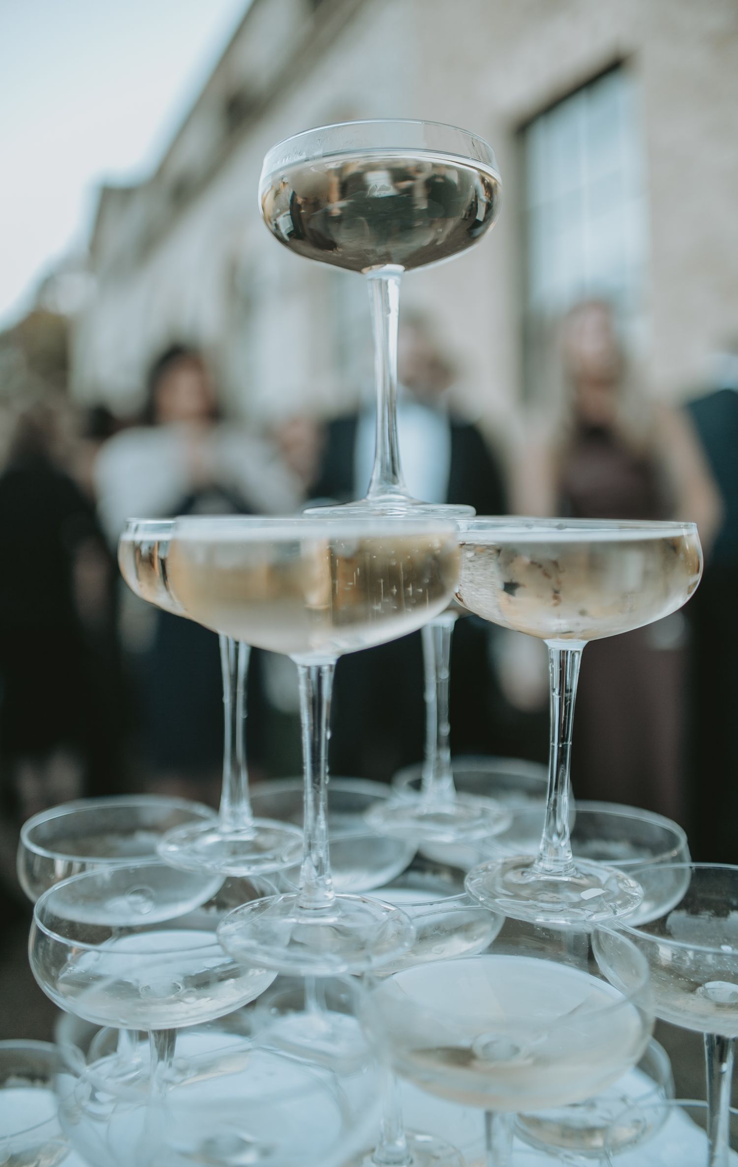 Close-up of vintage coupe glasses stacked in a tower formation at an outdoor event.