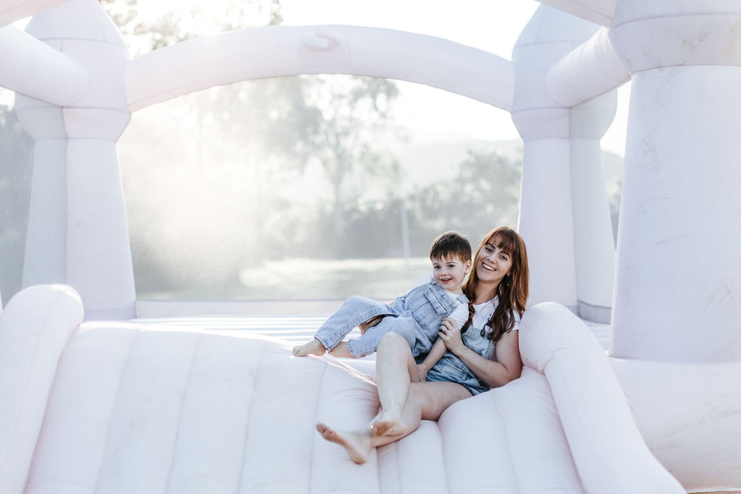 A playful moment captured in a white bounce house with soft natural lighting in the background.