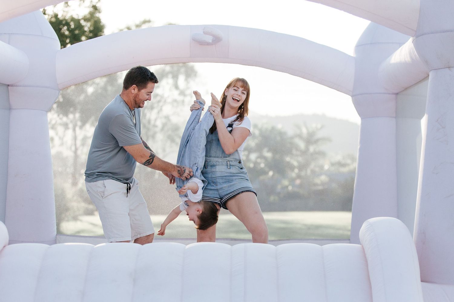 Playful family moment in a bright white bounce house with arched windows.
