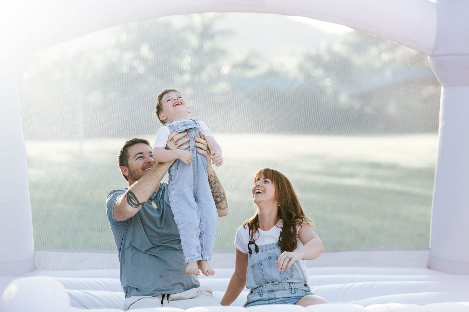 Candid family playtime photographed in a white bounce house with natural lighting.
