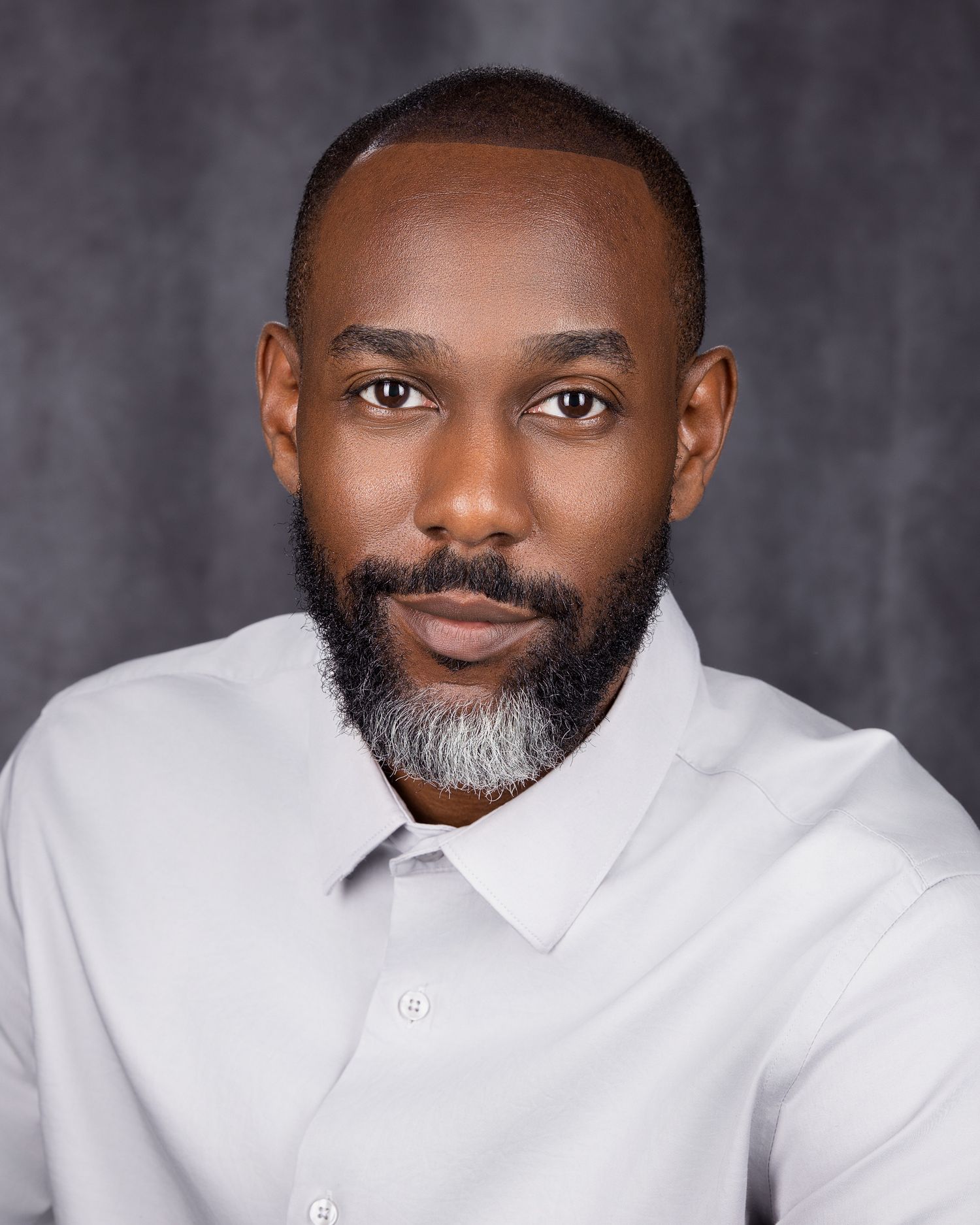 Professional headshot of a person wearing a crisp white button-down shirt against a dark grey background.