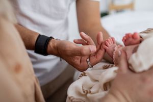 Gentle touch of tiny baby hands wrapped in rainbow patterned swaddle blanket.