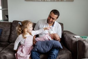 A family bonds together on a brown couch while meeting their new baby sibling.