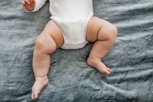 Close up view of a baby's chubby legs and diaper against gray linen bedding.
