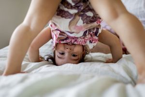 Playful scene of a child doing a somersault on white bedding.