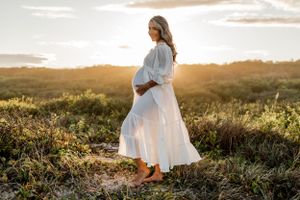 Flowing white dress catches breeze as woman poses in natural setting during sunset.