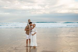 A family stands together in the shallow waters of a beach during sunset.