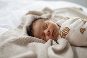 Close up of sleeping newborn baby wrapped in rainbow patterned swaddle on textured blanket.