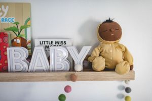 Nursery shelf displaying the word BABY and decorative items with pom pom garland.